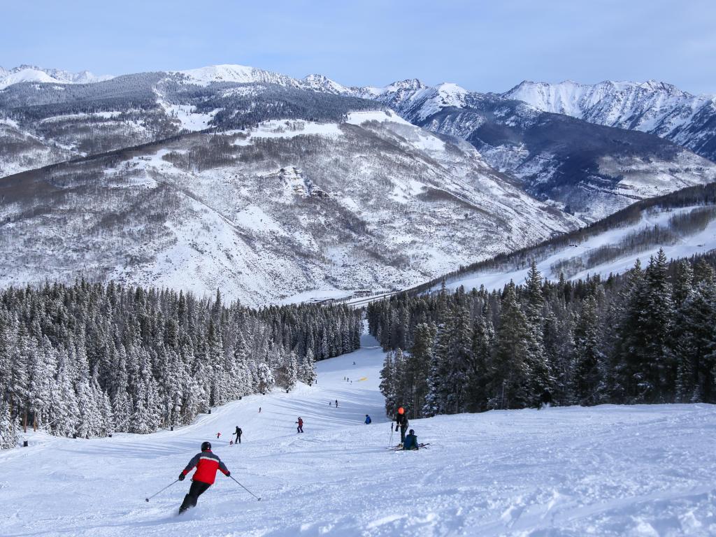 People skiing down the alpine slope in Colorado with snowy mountains in the distance