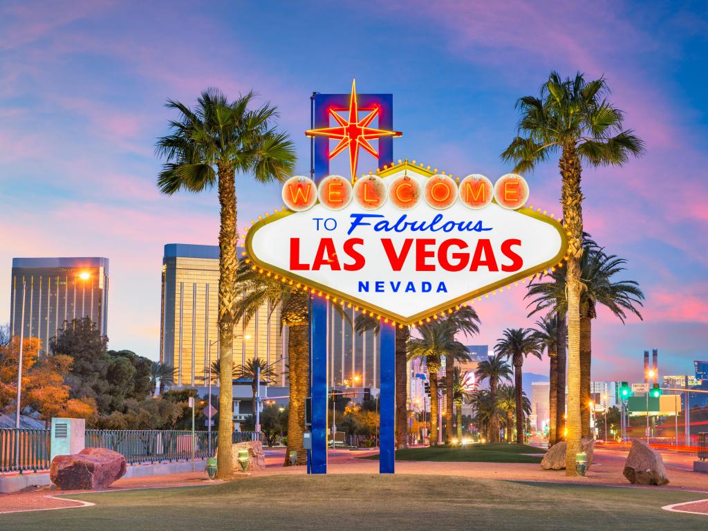 Neon Welcome to Las Vegas Sign with the city in the background. It's dusk and the sky has pink tones. 