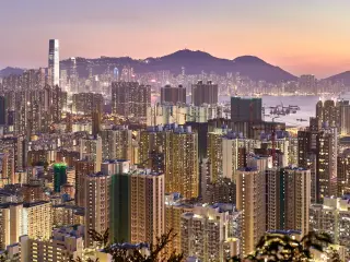 The Hong Kong skyline lit up amid a pink sunset with the harbour in the middle and mountains in the background