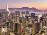 The Hong Kong skyline lit up amid a pink sunset with the harbour in the middle and mountains in the background