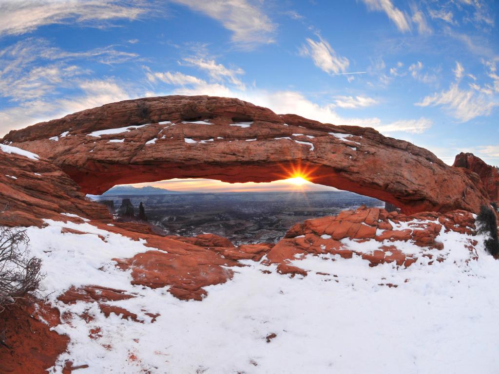 Sun shining through a natural arch in Canyonlands National Park, Utah, in winter, with snow all around