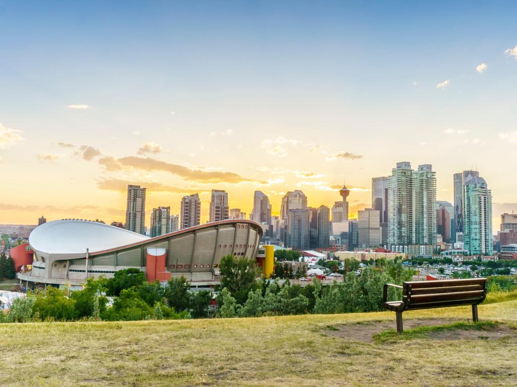 Calgary, Alberta, Canada with the downtown city at sunset during summertime, and a bench and grass area in the foreground.