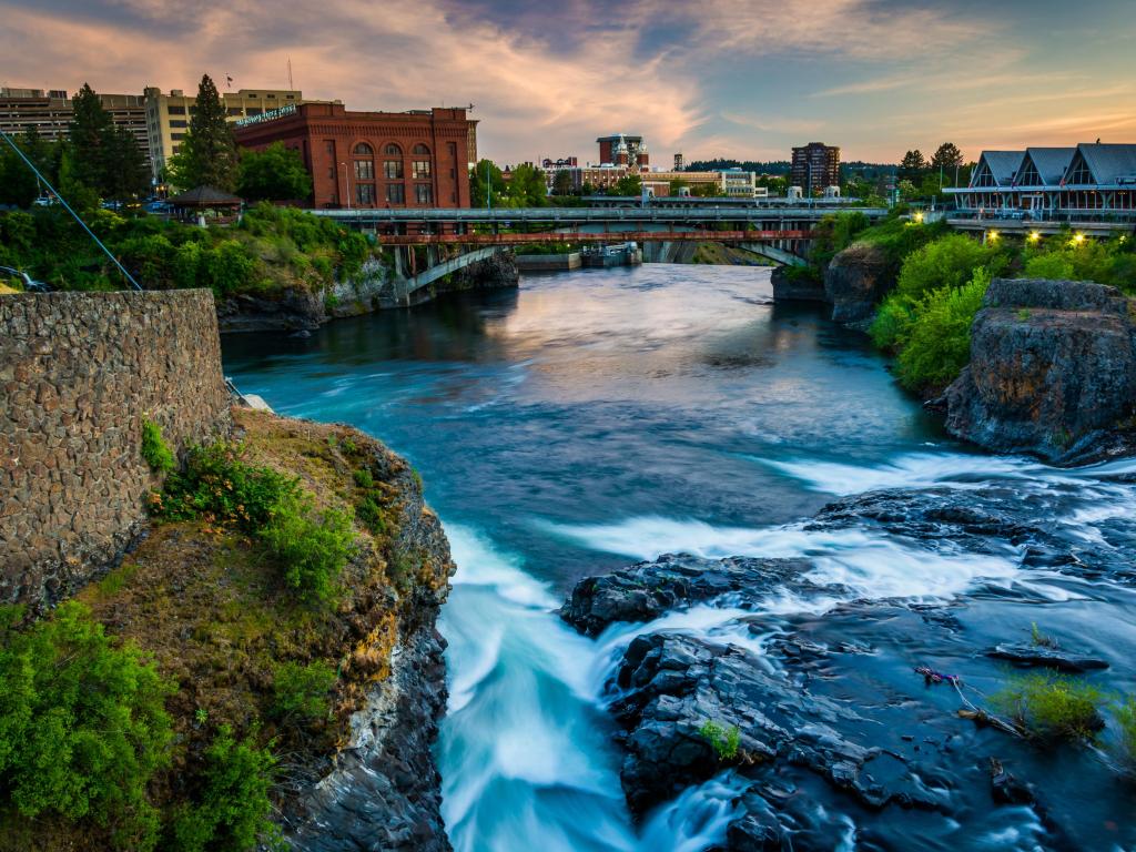 Spokane Falls, Spokane, Washington, USA with the waterfall in the foreground, a bridge and buildings in the distance taken at dusk. 
