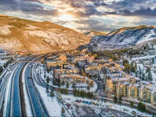 Aerial view of the road leading to Vail Colorado, with the snow topped mountains all around and sun shining through the clouds