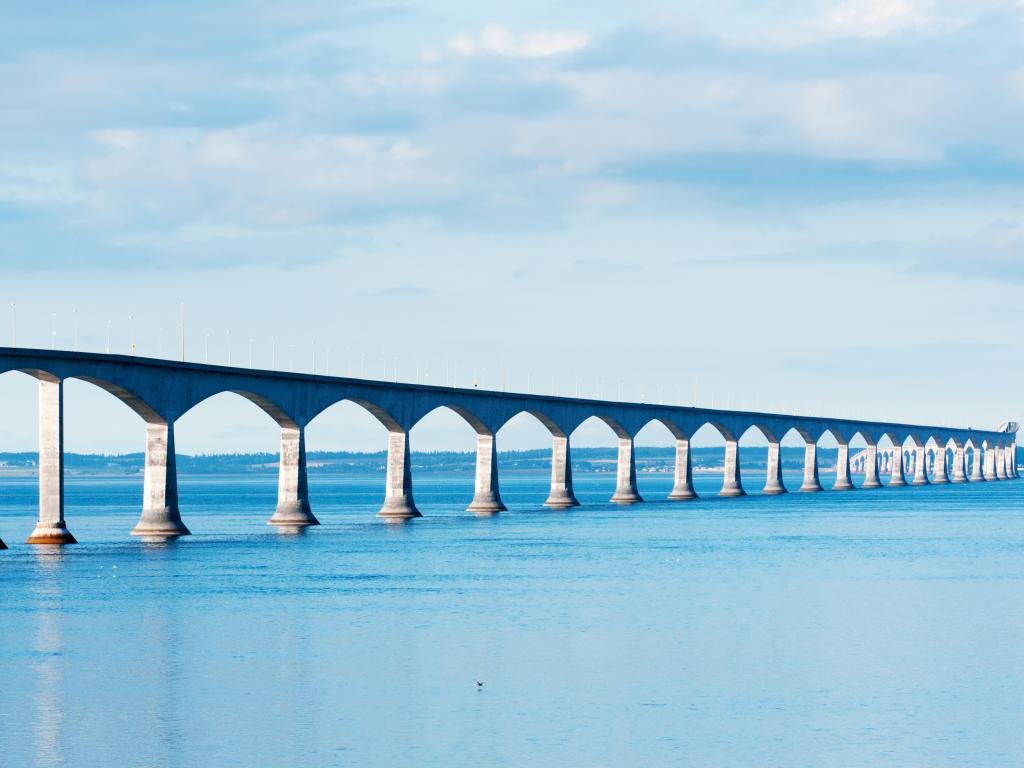 Long white bridge with many arches crossing wide blue sea with no land nearby