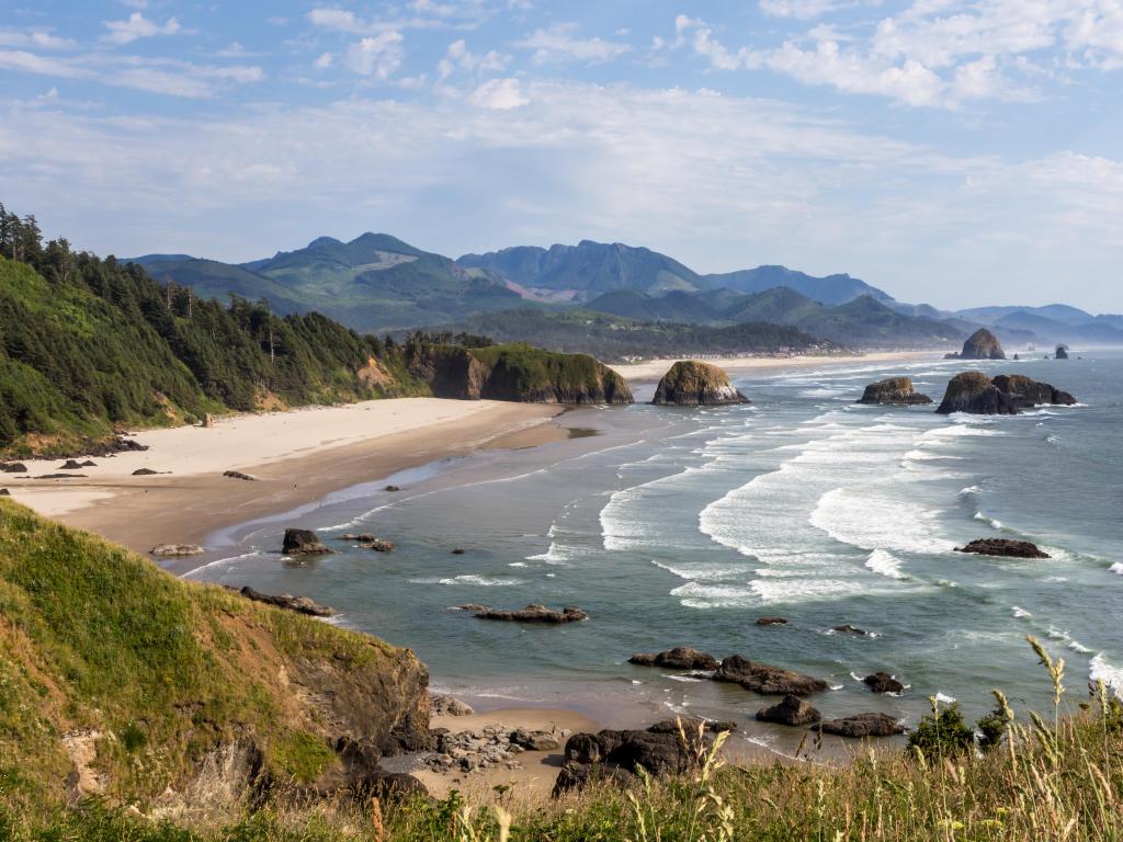 Cannon Beach, Ecola State Park, Oregon, USA with the pacific coast and a sandy beach surrounded by green hills and mountains in the distance taken on a sunny day.