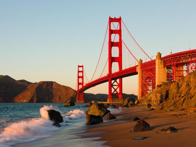 Golden Gate Bridge in San Francisco at sunset with waves crashing on the beach.