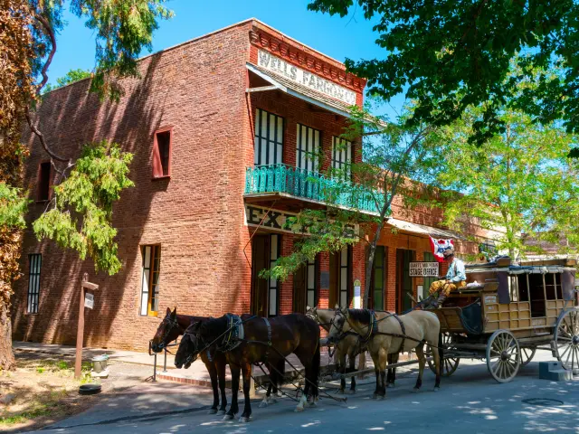 A horse-drawn antique stagecoach waits outside a historic building in Columbia, California on a sunny day