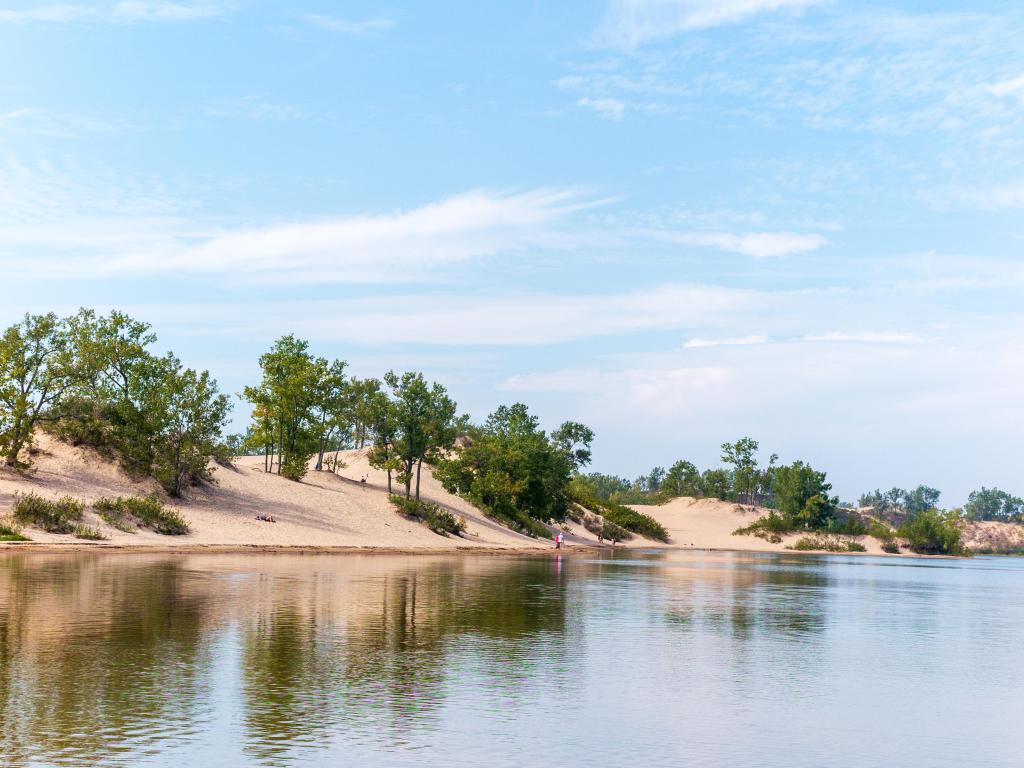 Sandbanks Provincial Park, Prince Edward County, Ontario with a beautiful sandy beach, dotted with trees, calm water and taken on a sunny day.