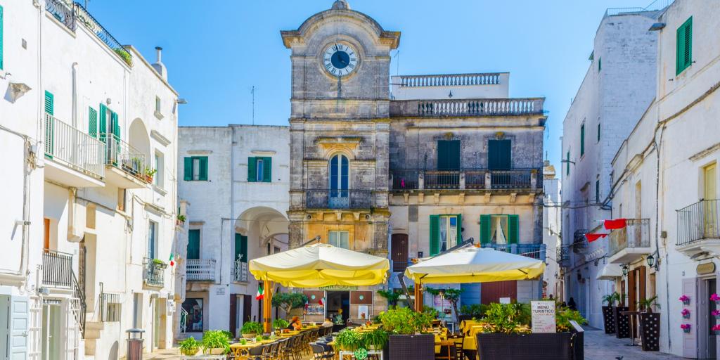 Cisternino clock tower with a cafe in front against a blue sky 