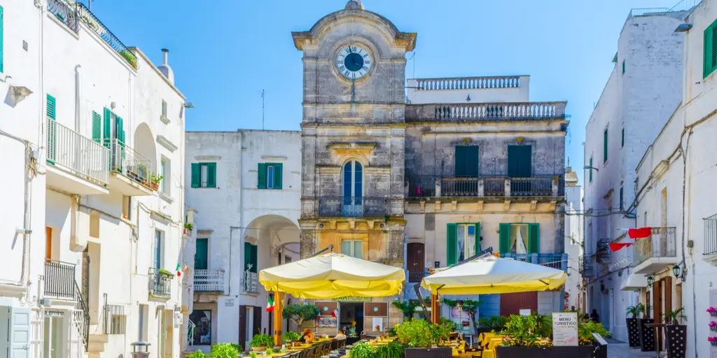Cisternino clock tower with a cafe in front against a blue sky 
