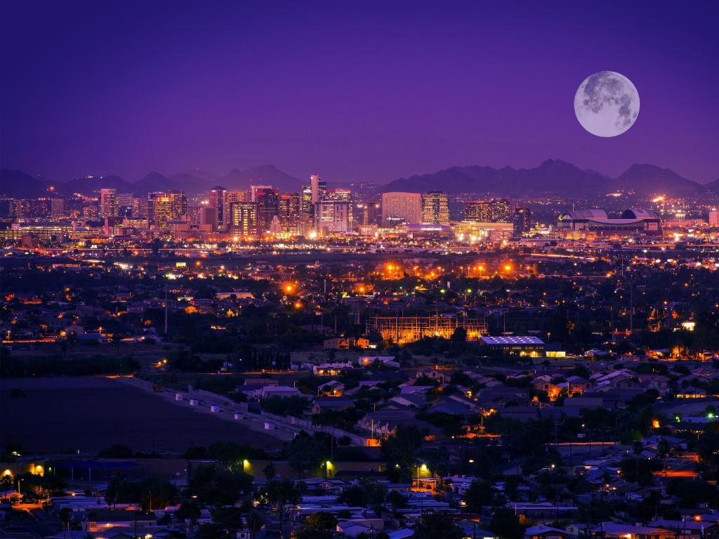 View of downtown Phoenix after dark with large moon and city lights reflecting on water