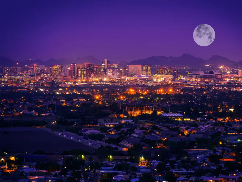 View of downtown Phoenix after dark with large moon and city lights reflecting on water