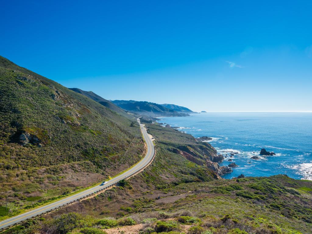 California State Route 1, with a road running alongside green mountains and the bright blue sea to the right.