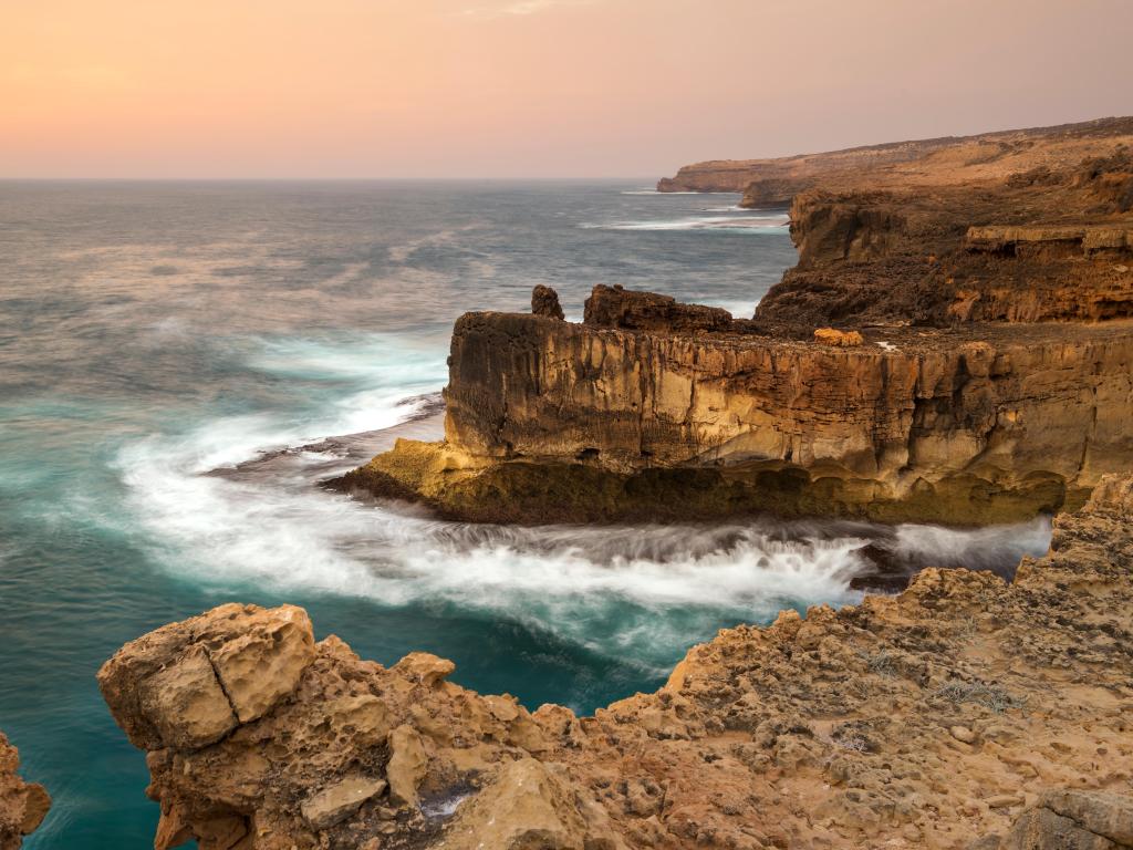 Mystical rocks formations with turbulent ocean crashing against the cliffs during sunset
