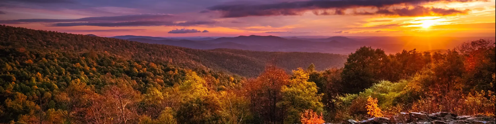 Shenandoah National Park, Virginia at Autumn with a sunset in the distance, rocks in the foreground and overlooking the national park below.