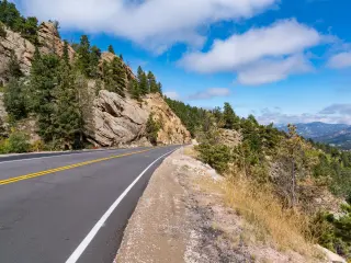 View of the scenic Peak to Peak Highway winding its way through the Rocky Mountains near Estes Park, Colorado with blue sky behind