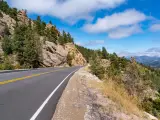 View of the scenic Peak to Peak Highway winding its way through the Rocky Mountains near Estes Park, Colorado with blue sky behind