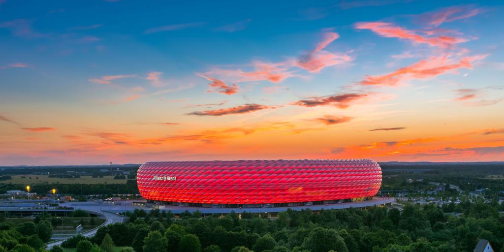 The bubbled exterior of the Allianz Arena lit up red with an orange sunset as a backdrop