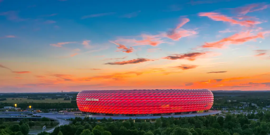 The bubbled exterior of the Allianz Arena lit up red with an orange sunset as a backdrop