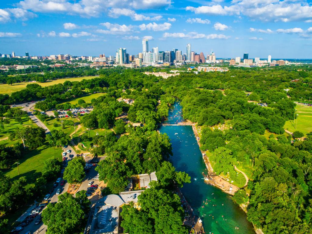 Barton Springs Pool with the skyline of Austin, Texas in the background and the natural outdoor pool in the foreground.