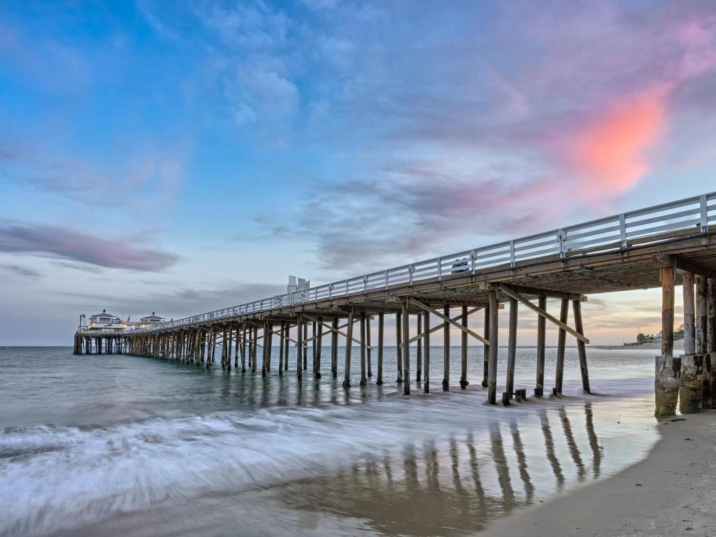 Malibu Pier in California at sunset with lights on the buildings at the end of the pier.