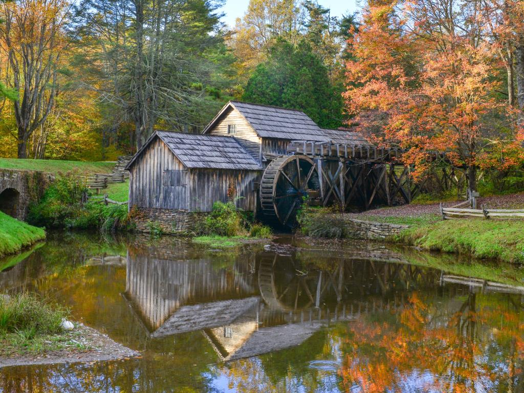 Old wooden watermill next to still pond surrounded by fall color trees