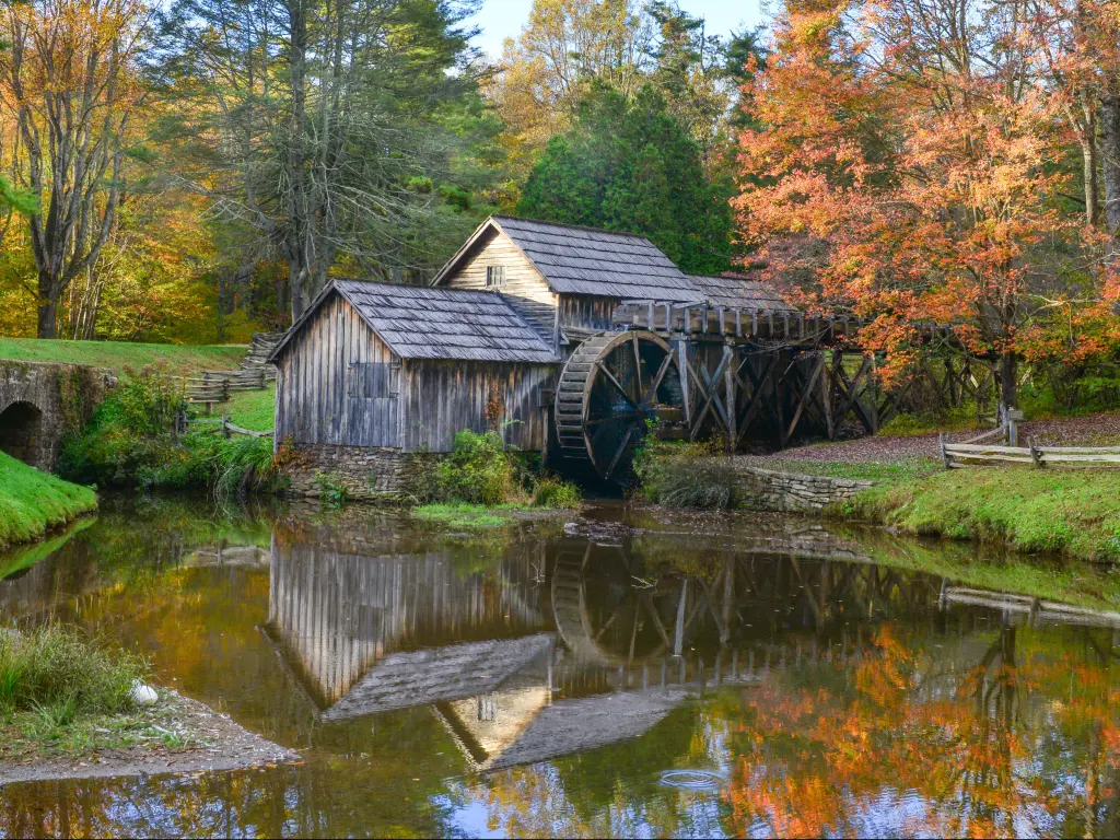 Old wooden watermill next to still pond surrounded by fall color trees