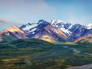 Denali National Park, Alaska with a road leading to snow-capped mountains in the distance on a clear day.