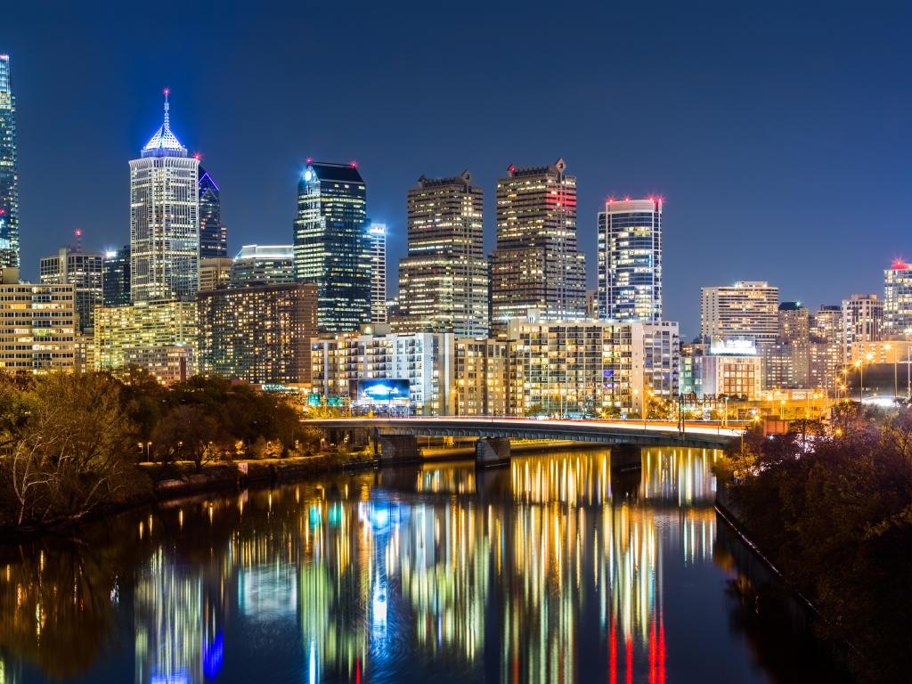Philadelphia, PA, USA with the cityscape panorama by night, the Schuylkill River reflecting the colorful skyscrapers in the foreground.
