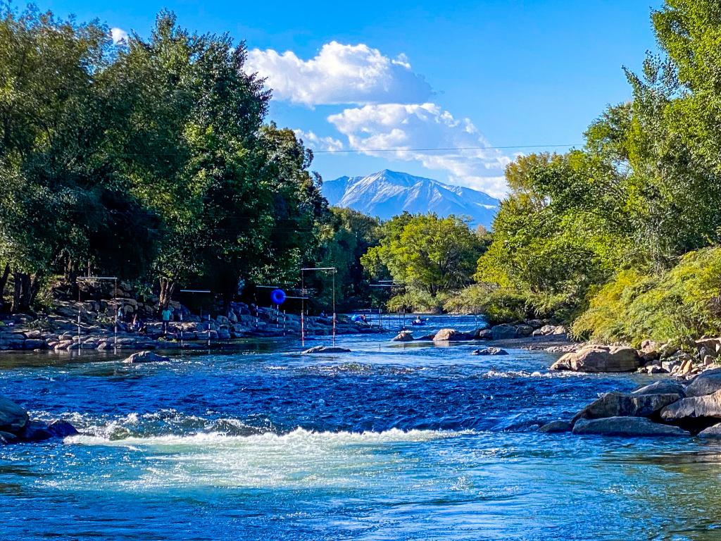 An image of the flowing Arkansas River near Salida, Colorado with trees and a mountain peak during a sunny day.