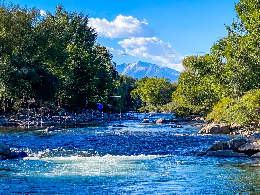 An image of the flowing Arkansas River near Salida, Colorado with trees and a mountain peak during a sunny day.