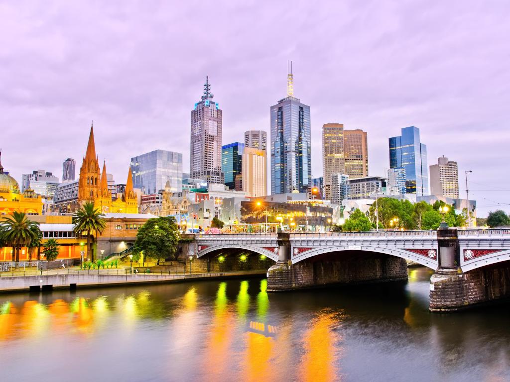 Highrise buildings of Melbourne skyline at dusk across river with bridge