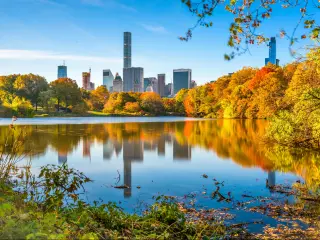 Central Park, New York City, USA during the fall with orange and yellow coloured trees, blue sky and the city skyline reflecting in the water. 