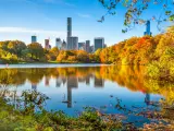 Central Park, New York City, USA during the fall with orange and yellow coloured trees, blue sky and the city skyline reflecting in the water. 