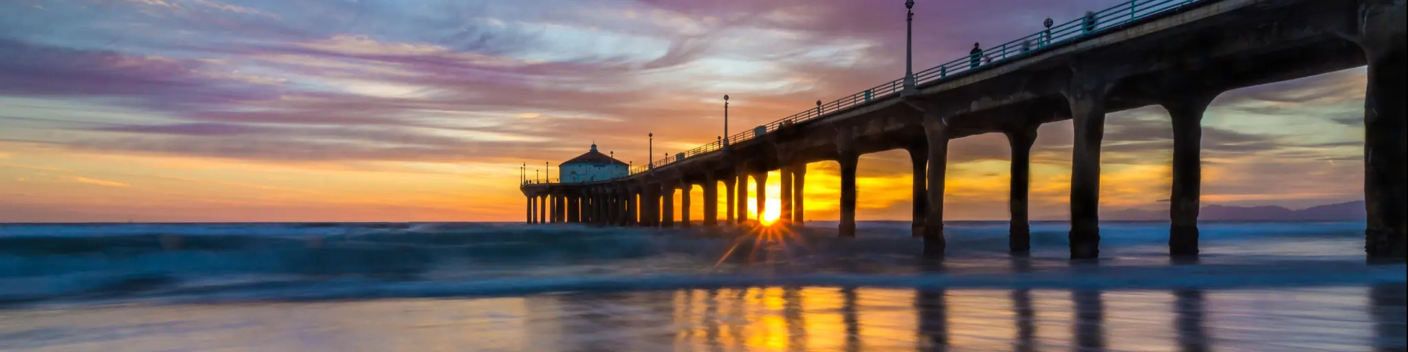 Manhattan Beach Pier, Los Angeles, USA with a long-exposure shot of the colorful sky and clouds over Manhattan Beach Pier at sunset with smooth waves washing onto the beach.