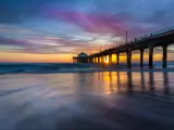 Manhattan Beach Pier, Los Angeles, USA with a long-exposure shot of the colorful sky and clouds over Manhattan Beach Pier at sunset with smooth waves washing onto the beach.