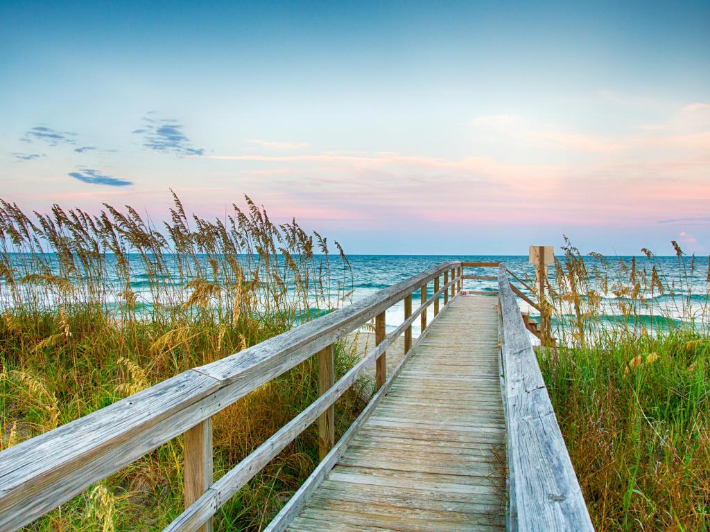 Board walk crosses sand dunes towards empty sandy beach and calm blue ocean