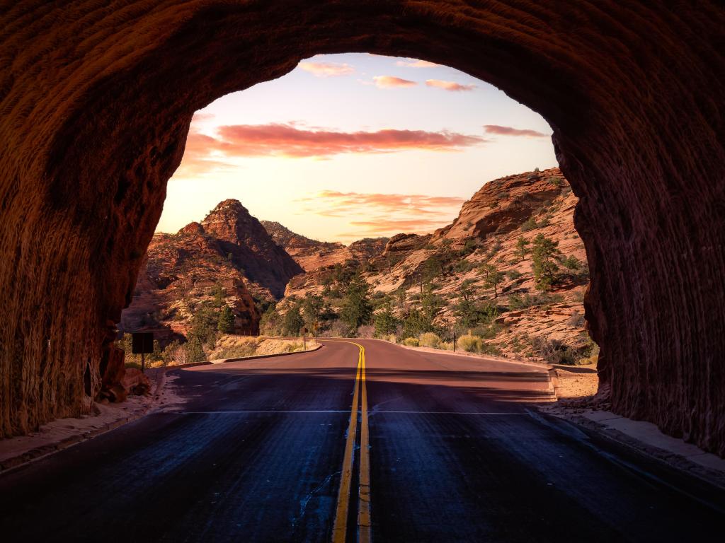 View of road and valley sides with a few trees, taken from a tunnel through the rocks 