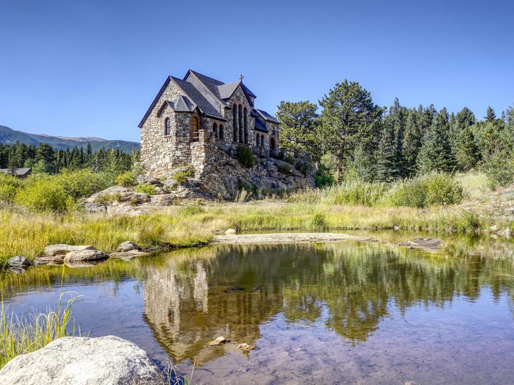 Catholic Saint Catherine's Chapel on the Rock perched next to a lake in Allenspark, Colorado, beneath a blue summer sky