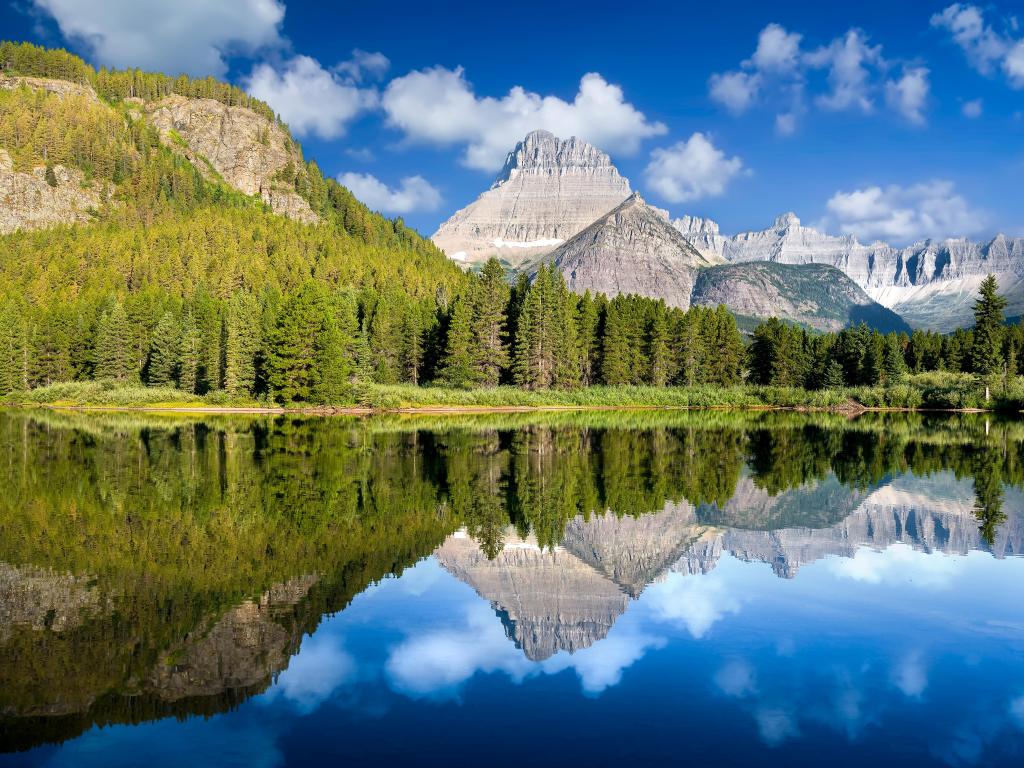 Glacier National Park, Montana, USA taken at Lake Josephine with peaceful calm reflections of the trees and mountains in the distance on a sunny day.