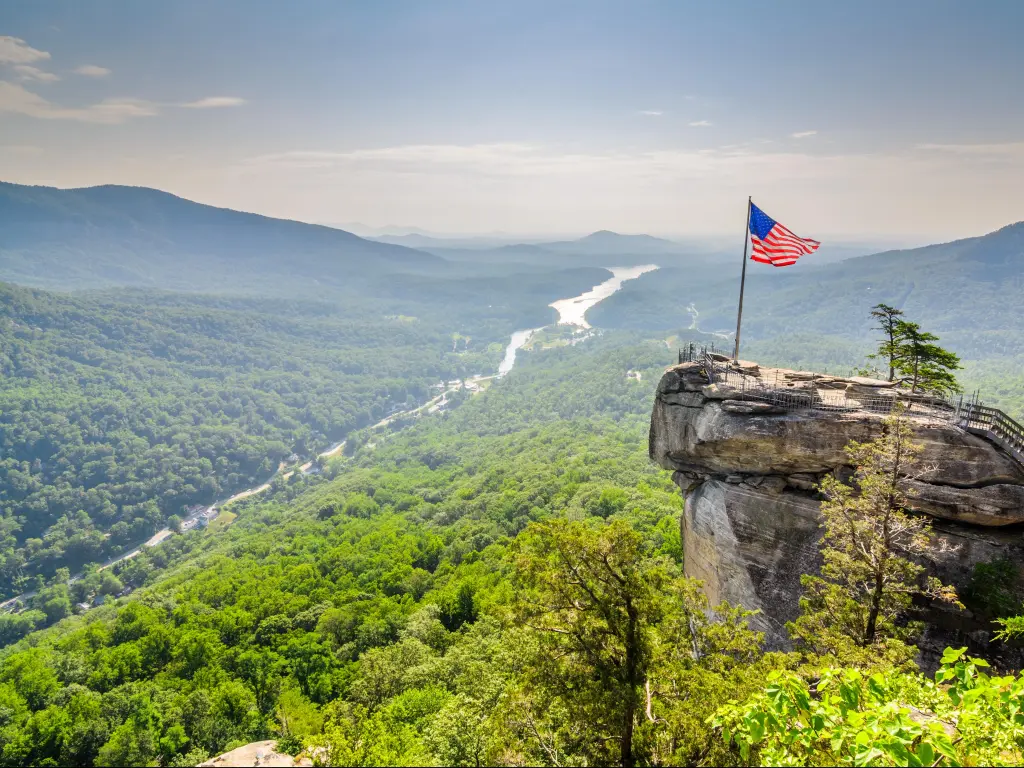 Chimney Rock at Chimney Rock State Park in North Carolina, USA with the US flag on top of the rock above a tree valley and hills.