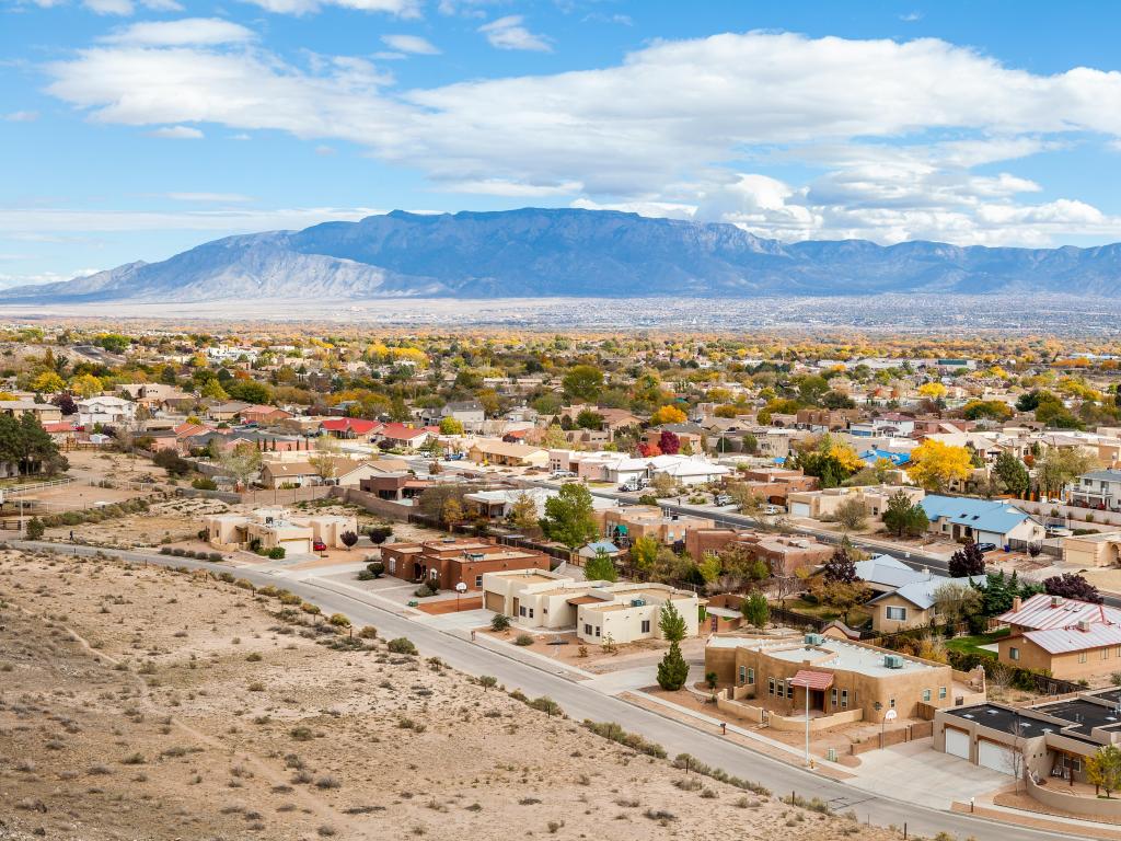 Albuquerque, New Mexico, USA with residential suburbs in the foreground and mountains in the distance on a sunny and cloudy day.