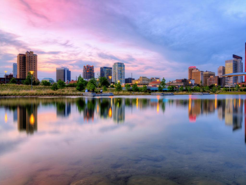 Birmingham, Alabama with calm water in the foreground reflecting the downtown skyline in the distance at sunset.