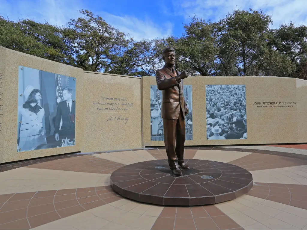 JFK Memorial in Dallas, with a statue in the center and historic photos behind, on a sunny day