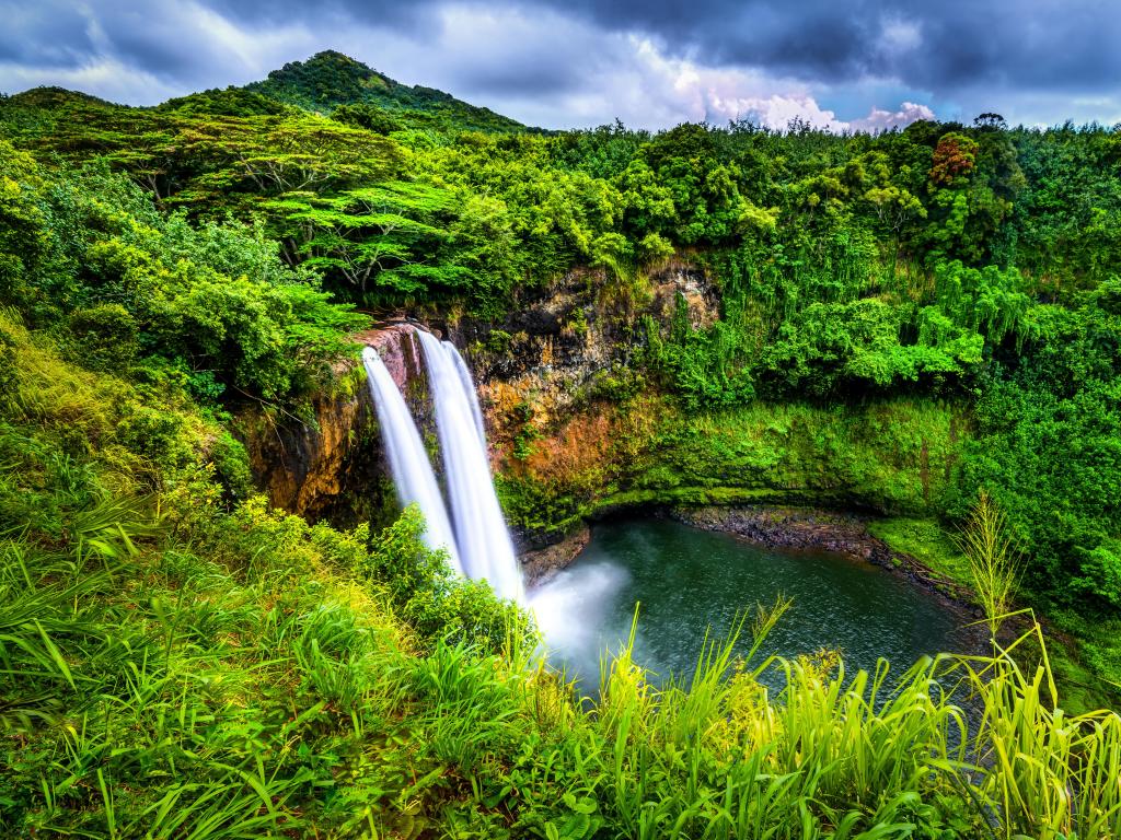Wailua Falls, Kauai, HI with greenery surrounding the impressive waterfall.