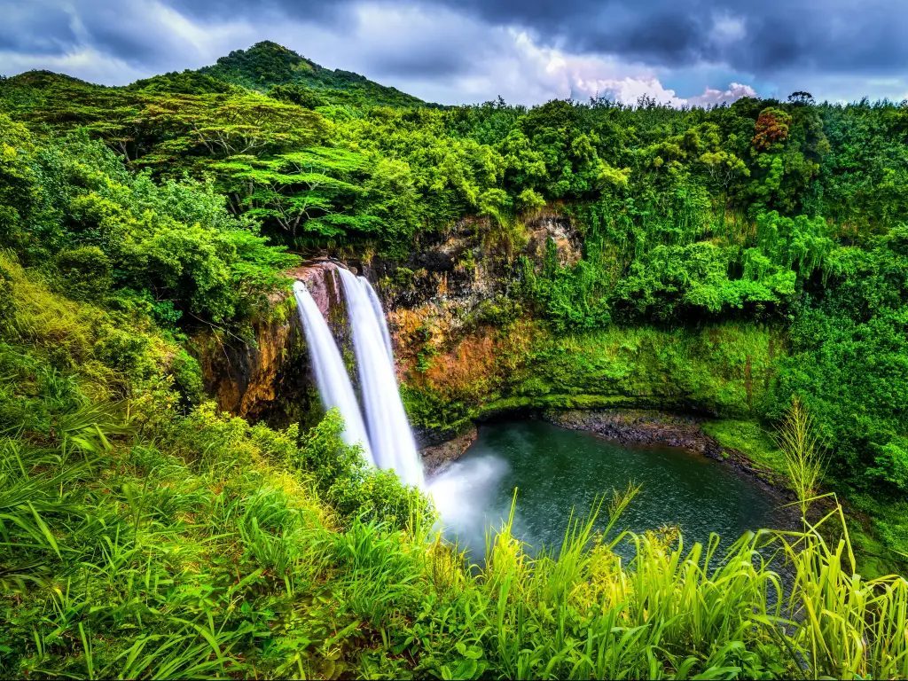 Wailua Falls, Kauai, HI with greenery surrounding the impressive waterfall.