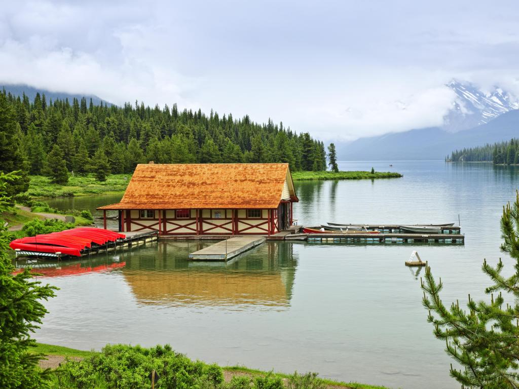 Red canoes lined up alongside the boathouse at Maligne Lake, with the lake and shoreline trees in the distance