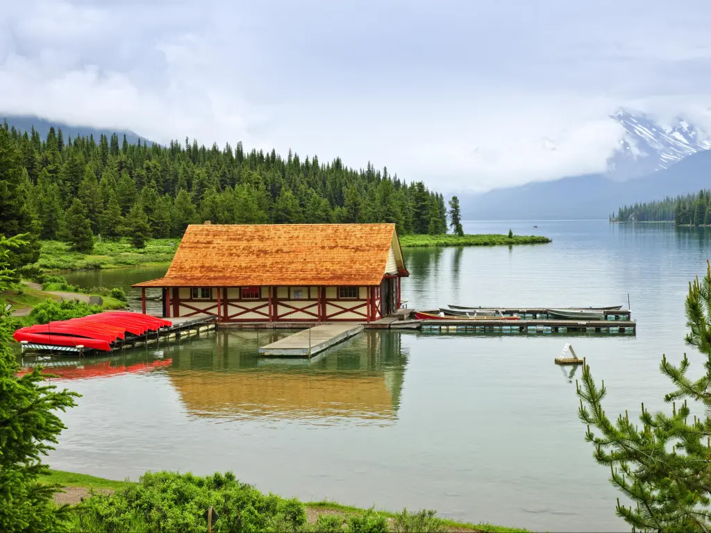 Red canoes lined up alongside the boathouse at Maligne Lake, with the lake and shoreline trees in the distance