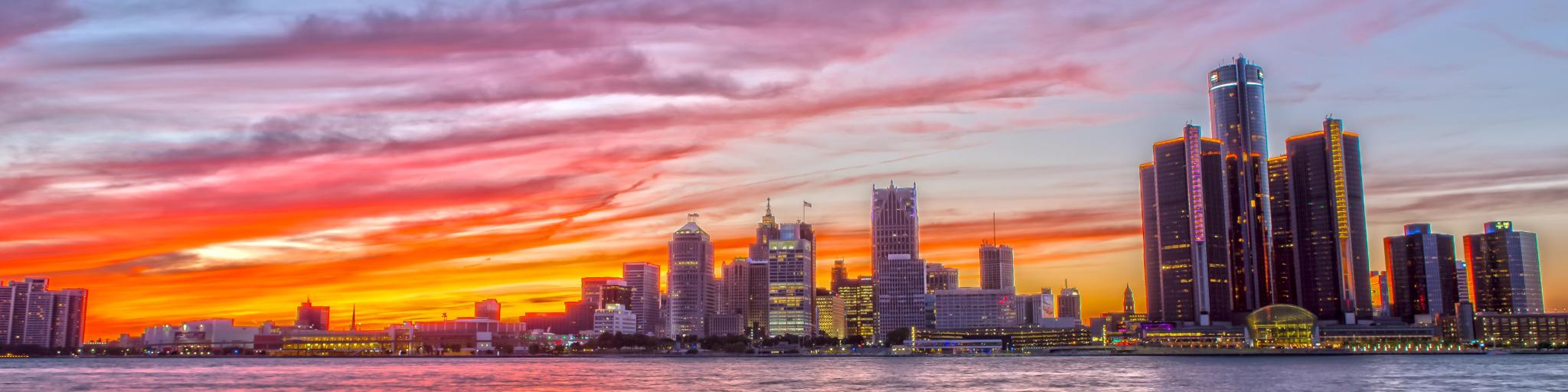 Detroit Skyline at sunset, with the river in the foreground and a purple-orange hued sky